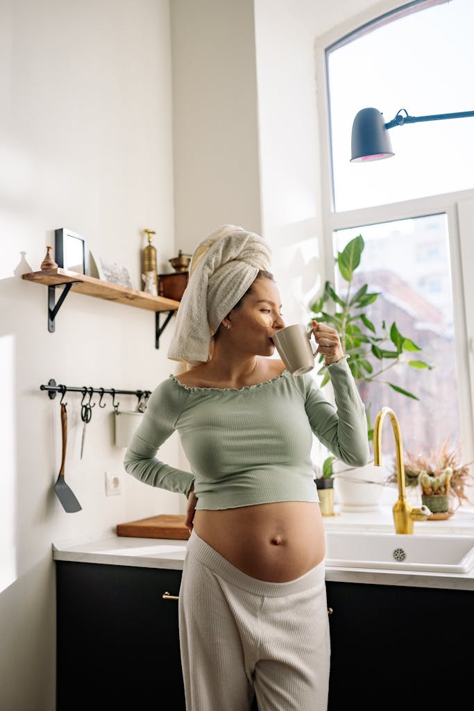 Pregnant woman in kitchen enjoying a hot drink, embracing relaxation and comfort.