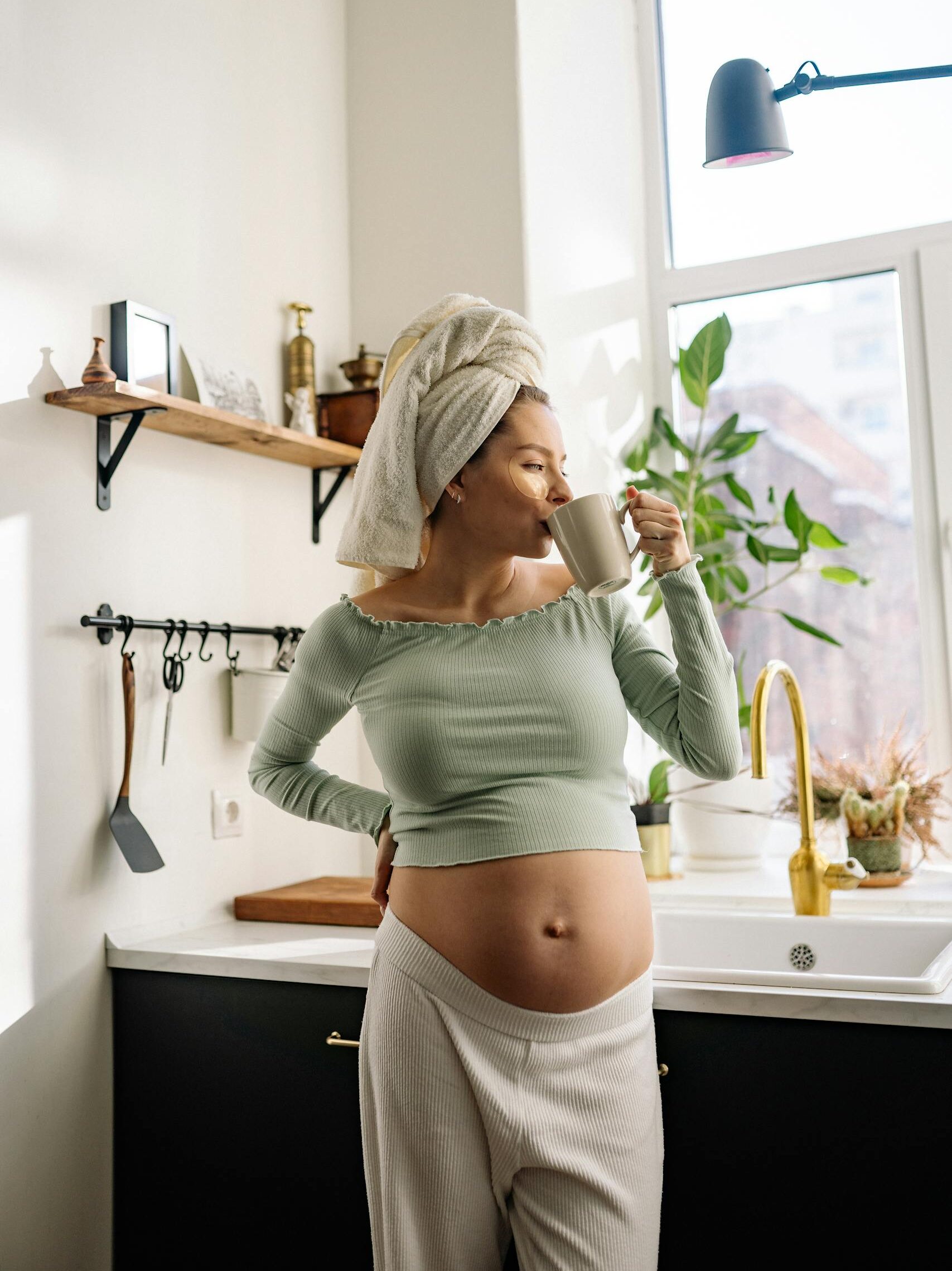 Pregnant woman in kitchen enjoying a hot drink, embracing relaxation and comfort.